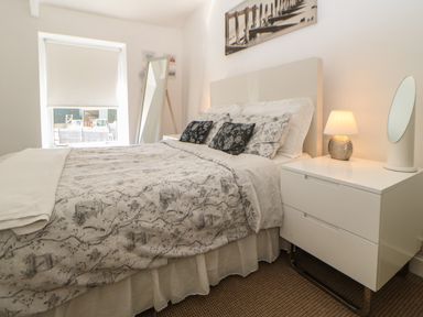 A bedroom with a bed with patterned bedding a bedside table with a lamp and mirror and a standing mirror near the window at Hollie Cottage in Haltwhistle