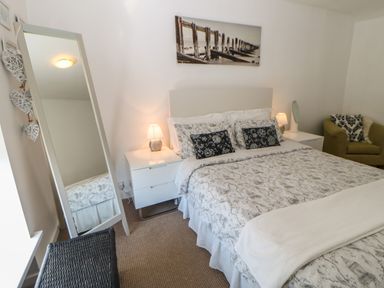 A bedroom with a double bed bedside tables lamps a full-length mirror and an armchair at Hollie Cottage in Haltwhistle