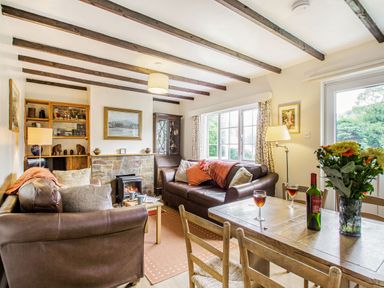 A living room with two brown leather sofas a wooden dining table with flowers and wine at Penlan in Beddgelert