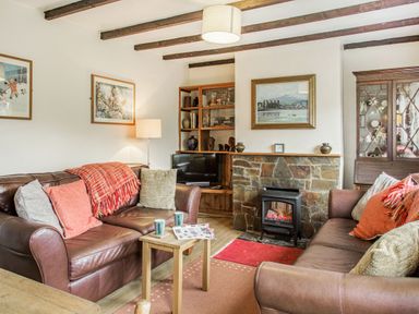 A living room with two brown leather sofas a wooden coffee table and a stone fireplace at Penlan in Beddgelert