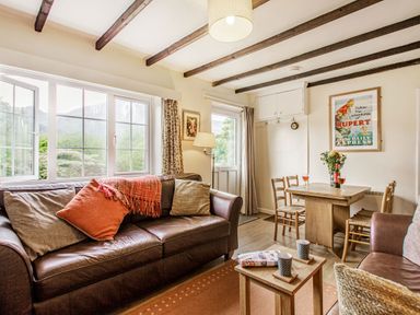 A living room with brown leather sofas cushions a wooden dining table with chairs and flowers on it at Penlan in Beddgelert
