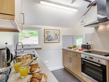 A kitchen with a countertop holding croissants, glasses of orange juice, bread, vegetables, an oven, a toaster, and a sink at Penlan in Beddgelert