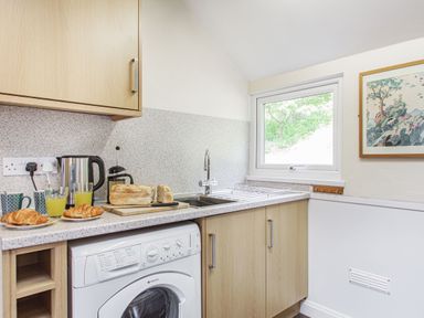 A kitchen counter with croissants juice loaf of bread coffee maker kettle and washing machine under the counter at Penlan in Beddgelert
