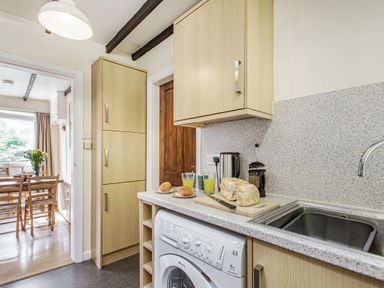 A kitchen countertop with bread, croissants, juice, and kitchen appliances next to a sink and washing machine at Penlan in Beddgelert
