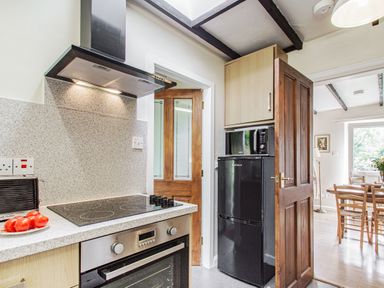A kitchen with an electric stovetop and oven a black refrigerator with a microwave on top and a door leading to a dining area at Penlan in Beddgelert