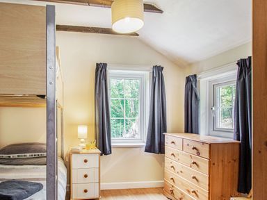A bedroom with bunk beds nightstand with lamp and dresser near two windows with curtains at Penlan in Beddgelert