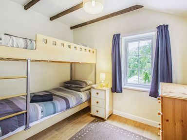 A bedroom with bunk beds a small nightstand with a lamp and glasses a window with curtains and a wooden dresser visible at Penlan in Beddgelert