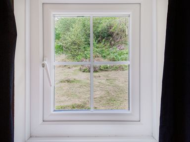 A window with white frame and black curtains showing grass and bushes outside at Penlan in Beddgelert
