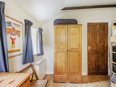 A room with a wooden wardrobe wooden door wooden chair a window with curtains and a framed poster on the wall at Penlan in Beddgelert