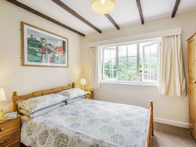 A bedroom with a double bed with floral bedding wooden side tables with lamps and a large window with curtains at Penlan in Beddgelert