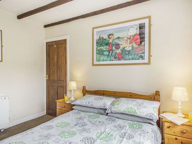 A bedroom with a wooden bed and floral bedding two bedside tables with lamps and drinks a wooden door and framed artwork on the wall at Penlan in Beddgelert
