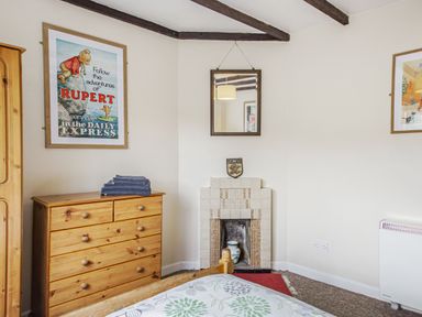 A bedroom with a wooden chest of drawers and wardrobe next to a tiled fireplace with a mirror above at Penlan in Beddgelert