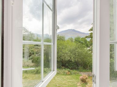 View through an open window showing trees bushes a grassy yard and a mountain in the background at Penlan in Beddgelert