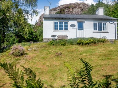 A white cottage with two chimneys and a railing in front surrounded by grass and trees at Penlan in Beddgelert