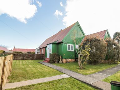 A green house with a red roof and a lawn with shrubs and a pathway at Cra-na-ge in Embleton