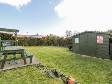 A backyard with a green picnic table a large green shed and a small garden bed at Cra-na-ge in Embleton
