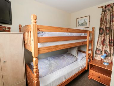 A bedroom with a wooden bunk bed a wooden nightstand with a small blue lamp a wooden cabinet a wall-mounted television and a framed picture on the wall at Cra-na-ge in Embleton