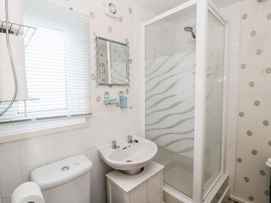 A bathroom with a shower cubicle a sink and a toilet under a window at Cra-na-ge in Embleton