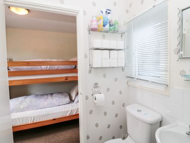 A bathroom with a toilet and sink and a view into a room with a bunk bed at Cra-na-ge in Embleton