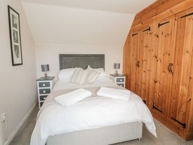 A bedroom with a double bed flanked by two bedside tables with lamps and a wooden wardrobe along one wall at Cra-na-ge Embleton