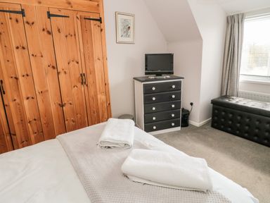 A bedroom with wooden wardrobes a black chest of drawers with a TV and a black bench near a window at Cra-na-ge in Embleton