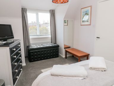 A bedroom with a bed with folded towels a black television on a dresser a black leather storage bench a wooden bench a wall mirror and a window with curtains at Cra-na-ge Embleton