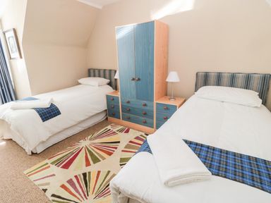 A bedroom with two single beds a blue wardrobe a colorful rug and bedside lamps at Cra-na-ge in Embleton