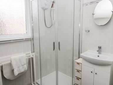 A bathroom with a shower cubicle towels on a rack a sink with cabinet and a round mirror at Cra-na-ge Embleton