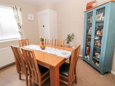 A dining room with a wooden table and six chairs a glass cabinet and a window at Cra-na-ge in Embleton