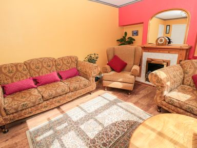 A living room with patterned sofas an armchair a rug a wooden coffee table a fireplace and a mirror at Cra-na-ge in Embleton