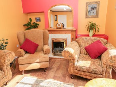A living room with two armchairs and a fireplace with a mirror above at Cra-na-ge in Embleton