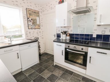 A kitchen with white cabinets black countertops an oven a stove a dishwasher a sink a window and a door at Cra-na-ge in Embleton