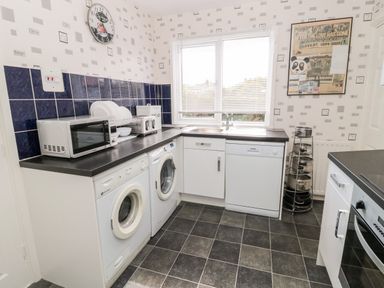 A kitchen with washing machine microwave wall clock and window at Cra-na-ge in Embleton