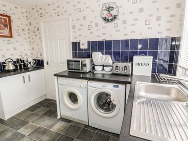 A kitchen with a washing machine, microwave, toaster, sink, drying rack, and tiled walls at Cra-na-ge Embleton