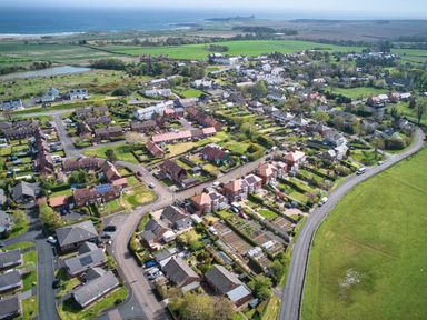 An aerial view of a residential neighborhood with houses gardens roads and fields near the coast at Cra-na-ge in Embleton