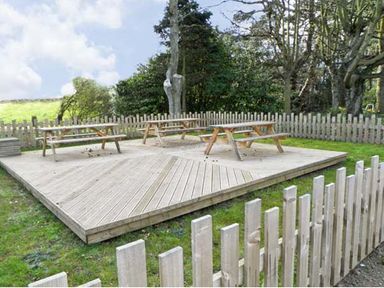 A wooden deck with picnic tables surrounded by a wooden fence in a grassy area with trees at No 1 Low Hall Cottages Scalby near Scarborough
