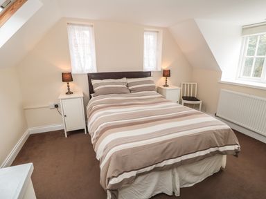 A bedroom with a double bed striped bedding two bedside tables with lamps a white chair and two small windows at No 1 Low Hall Cottages Scalby near Scarborough