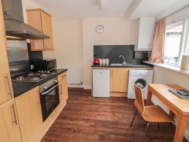 A kitchen with wooden cabinets a gas stove oven microwave small fridge washing machine and a wooden table with a chair at No 1 Low Hall Cottages Scalby near Scarborough