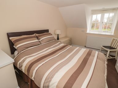 A bedroom with a double bed with striped bedding a bedside table lamp a window and a chair at No 2 Low Hall Cottages Scalby near Scarborough