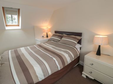 A bedroom with a double bed with striped bedding two bedside tables and two lamps at No 2 Low Hall Cottages Scalby near Scarborough