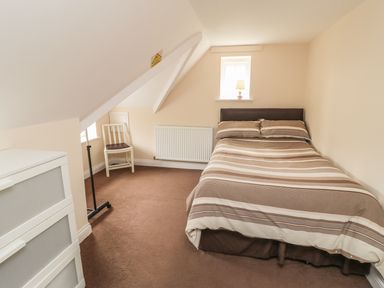 A bedroom with a double bed chair small window lamp and storage drawers at No 2 Low Hall Cottages Scalby near Scarborough