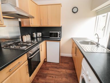 A kitchen with wooden cabinets a gas stove oven microwave kettle toaster small fridge sink and washing machine at No 2 Low Hall Cottages Scalby near Scarborough