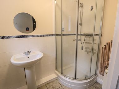 A bathroom with a pedestal sink a round mirror a corner shower enclosure with sliding glass doors and a towel rack with towels at No 2 Low Hall Cottages Scalby near Scarborough