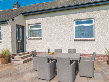 An outdoor patio with a rectangular table and six chairs in front of a house at Colt Park Cottage in Ulverston