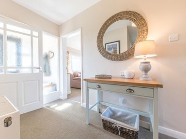 A hallway with a table lamp a wicker basket and a round mirror at Colt Park Cottage in Ulverston