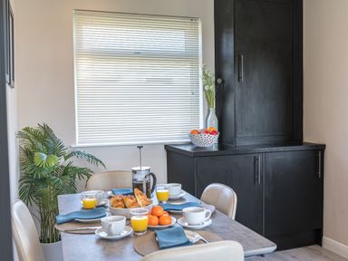 A dining room table set with cups juice croissants and tangerines next to a cabinet with fruit bowl and vase at Colt Park Cottage in Ulverston