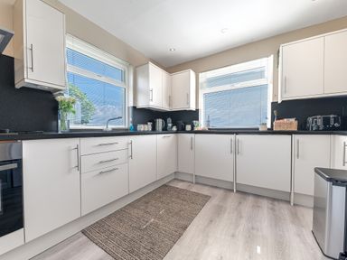 A kitchen with white cabinets black countertops appliances and two windows with blinds at Colt Park Cottage in Ulverston