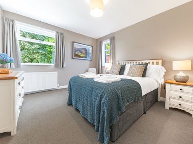 A bedroom with a double bed bedside tables lamps and a dresser with a vase of flowers at Colt Park Cottage in Ulverston