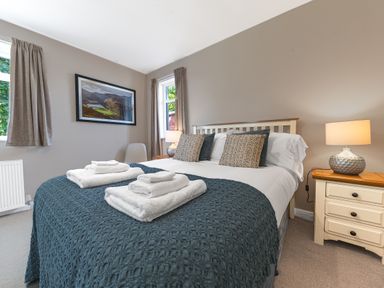 A bedroom with made bed with towels on it two bedside tables and a landscape picture on the wall at Colt Park Cottage in Ulverston