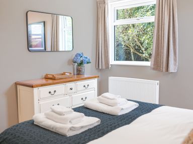 A bedroom with a white dresser a mirror window with curtains and towels on a bed at Colt Park Cottage in Ulverston